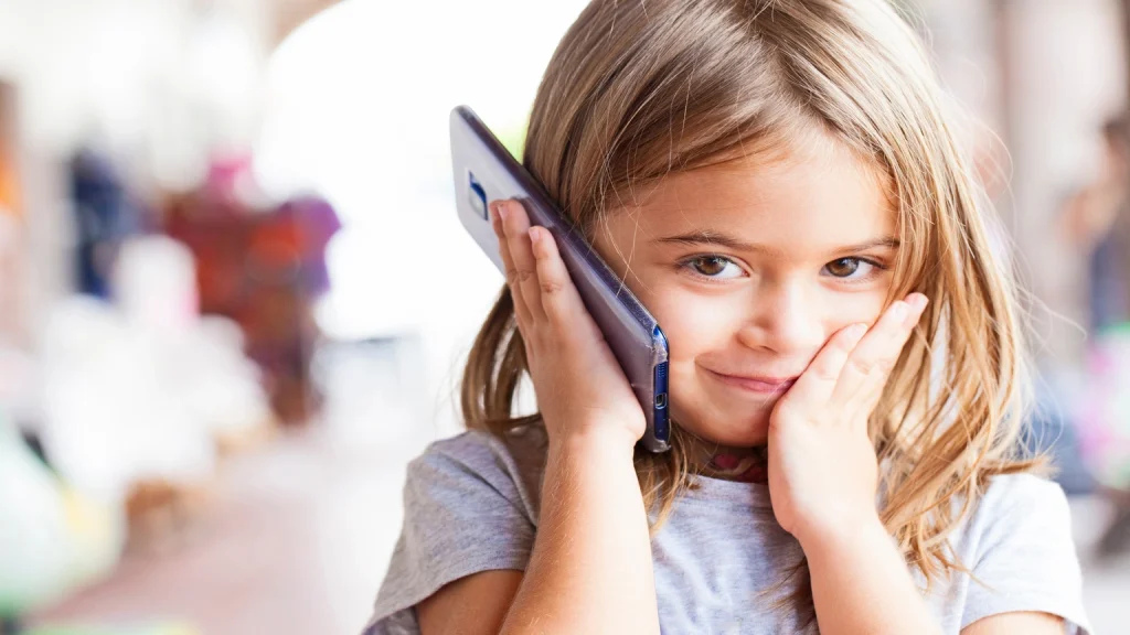 Ein junges Mädchen hält ein HTC-Smartphone an ihr Ohr und schaut konzentriert nach vorne. Im Hintergrund ist ein unscharfer neutraler Hintergrund zu erkennen.